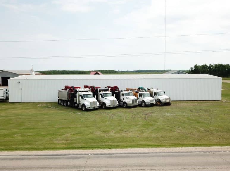 Row of diagonally parked hydrovacs in front of a metal industrial building.